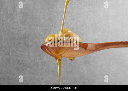 Les flux de l'huile d'olive vierge sur une cuillère en bois plein d'olives vert frais Banque D'Images