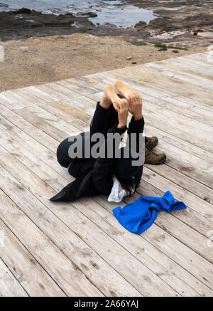 Espagnol mature woman stretching, performing Yoga on Beach Boardwalk. Banque D'Images