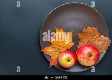 Vue de dessus de pommes rouges et de feuilles aux couleurs automnales est posé sur une plaque brune, sur un fond gris foncé. Vue de dessus avec l'espace pour le texte. Banque D'Images