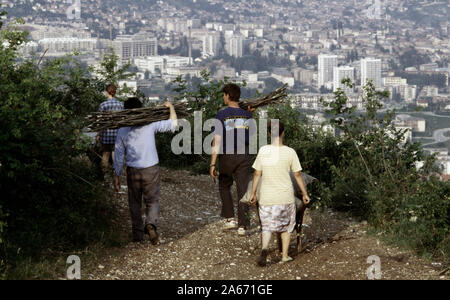 6 juin 1993 pendant le siège de Sarajevo : hommes et femmes portent le bois fraîchement coupé une piste près du haut de la colline de ronflement. Sarajevo est située en dessous d'eux, à l'est, avec le centre clinique universitaire de Sarajevo, connu sous le nom de Hôpital Koševo, directement au-delà d'eux. Banque D'Images