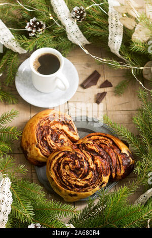 Muffins au chocolat escargot servi avec du café sur l'arrière-plan d'une couronne de branches de sapin et les cônes. Style rustique. Banque D'Images