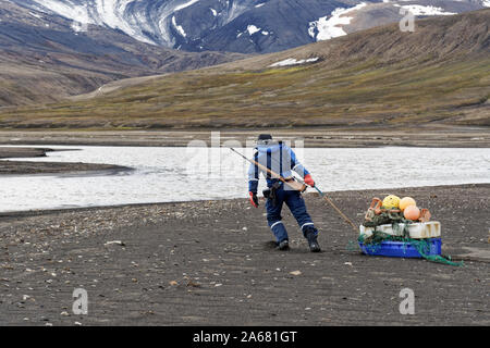 Plastiques près du pôle Nord : campagne de nettoyage Svalbard de Sysselmannen. Un volontaire tire les ordures vers un point de collecte, Agardhbukta, Svalbard, Norvège Banque D'Images