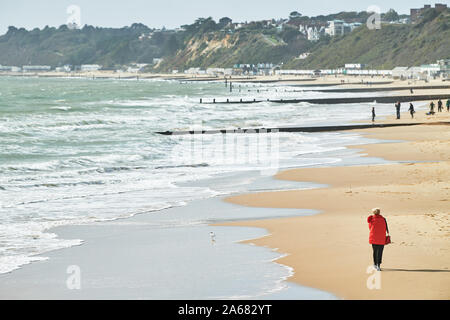 Une femme seule promenades le long du rivage d'une plage de sable au bord de la manche à Bournemouth, Angleterre. Banque D'Images