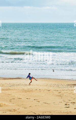 Un jeune garçon joue au football sur une plage de sable de la manche à Bournemouth, Angleterre. Banque D'Images