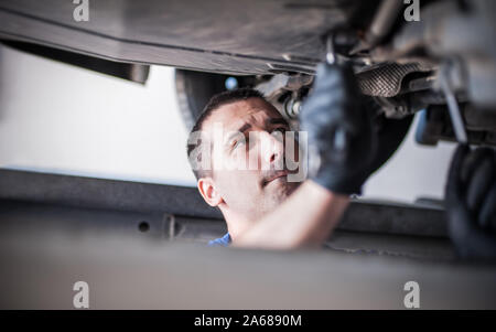 Mécanicien réparateur automobile Maître technicien de contrôle de l'état sous la voiture, sur l'ascenseur du véhicule en atelier Banque D'Images