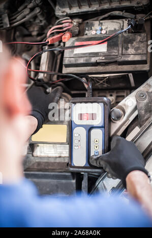 Location de maître mécanicien réparateur automobile contrôle et essai avec l'accumulateur batterie électronique numérique testeur et analyseur en atelier véhicule auto Banque D'Images