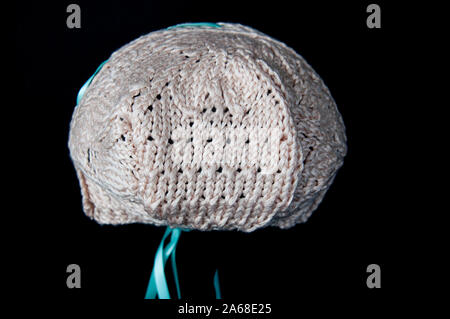 Dos de bébé écru bonnet avec rubans de satin de couleur aqua. Fibre art handknit accessoire bébé avec des points de suture, isolé sur un fond noir. Banque D'Images