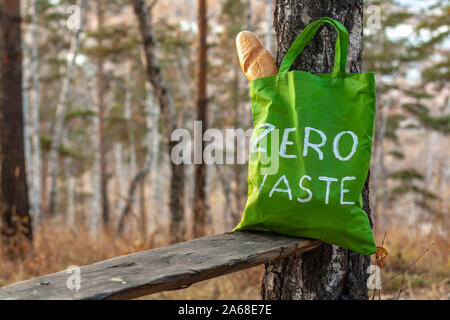 Sac vert textile avec inscription zéro déchet sur un fond de nature. Pain français dans un sac. Mise au point sélective. Arbres flous et herbe d'automne Banque D'Images