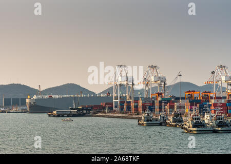 Port de Laem Chabang, Thaïlande - Mars 17, 2019 : grand grand navire de transport véhicules gris derrière container terminal avec ses grues et des piles de couleur Banque D'Images