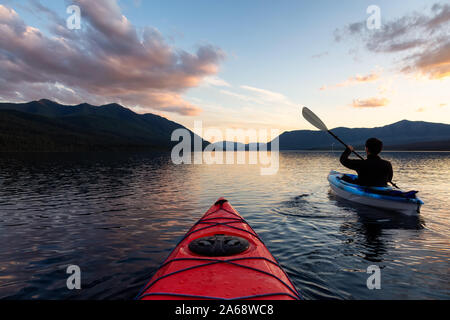 Homme aventureux Kayak dans le lac McDonald lors d'un coucher de soleil d'été ensoleillé avec les Montagnes Rocheuses en arrière-plan. Prises dans le parc national des Glaciers Banque D'Images