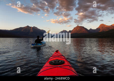 Homme aventureux Kayak dans le lac McDonald lors d'un coucher de soleil d'été ensoleillé avec les Montagnes Rocheuses en arrière-plan. Prises dans le parc national des Glaciers Banque D'Images