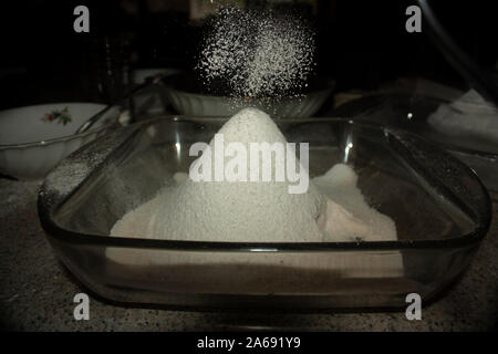 La farine d'Amande particules tamisée tombant lentement formant volcan avec verre de sucre et de farine d'amande Banque D'Images