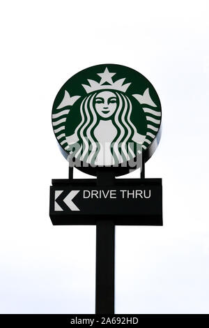 Un signe extérieur contre un fond de ciel gris pour un Starbucks Drive avec le logo Starbucks au-dessus de la route à travers. Banque D'Images