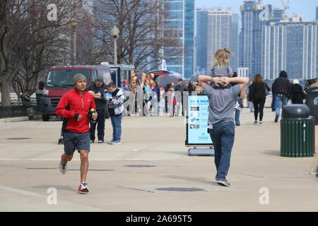 Chicago, Illinois / USA - Mars 28, 2018 : Père donne une fille piggyback ride et l'homme s'en va pour un jogging à la Chicago Riverwalk Banque D'Images