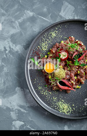 Tartare de boeuf servi dans une plaque noire ronde sur un sombre bureau, vue d'en haut. Banque D'Images