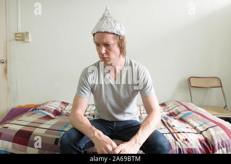 Jeune homme a souligné avec du papier d'aluminium hat pensant dans la chambre à coucher Banque D'Images
