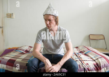 Jeune homme a souligné avec du papier d'aluminium hat pensant dans la chambre à coucher Banque D'Images