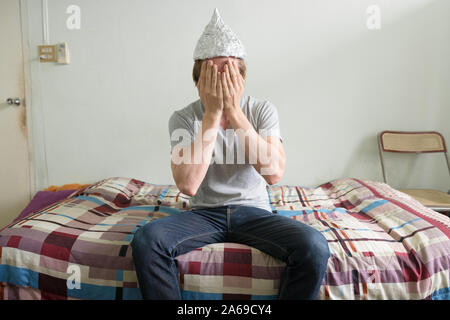 Jeune homme a souligné avec tin foil hat covering face dans la chambre à coucher Banque D'Images