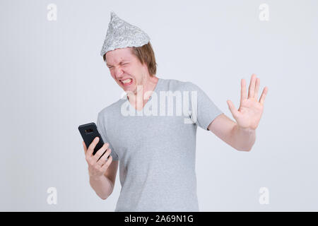 Jeune homme a souligné avec du papier d'aluminium hat en utilisant le téléphone et à la peur Banque D'Images