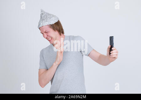 Jeune homme a souligné avec du papier d'aluminium hat en utilisant le téléphone et à la peur Banque D'Images