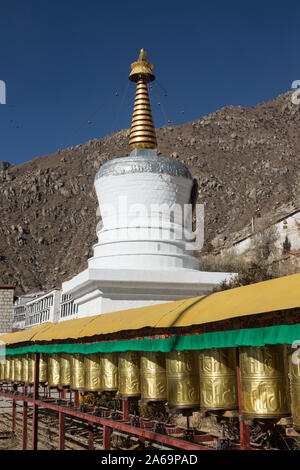 Une rangée de roues de prière en face d'un stupa bouddhiste au Monastère Drepung, près de Lhassa, au Tibet. Banque D'Images
