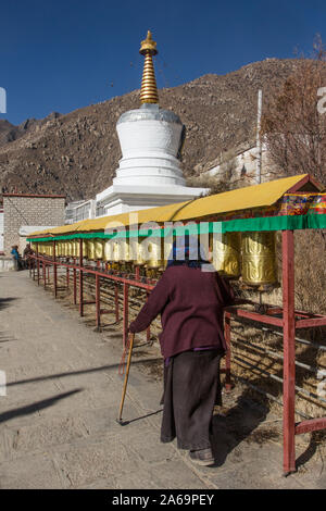 Un adorateur tourne roues de prière en face d'un stupa bouddhiste au Monastère Drepung, près de Lhassa, au Tibet. Banque D'Images
