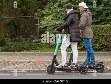 Deux garçons sur les scooters électriques filmé avec effet panoramique en mouvement sur un fond de plantes vertes Banque D'Images