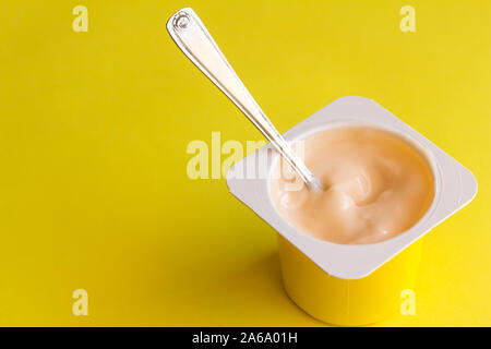 Du yogourt en pot en plastique avec petite cuillère isolé sur fond jaune Banque D'Images