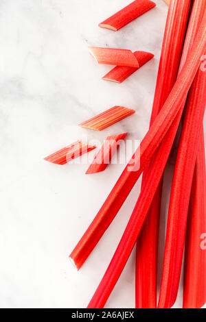 Vue de dessus de la rhubarbe forcée des matières premières et de tiges de rhubarbe coupées en morceaux de marbre blanc avec copie espace. Banque D'Images