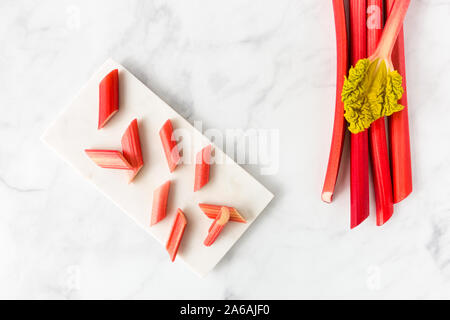 Couper les jeunes la rhubarbe forcée sur pièces en planche à hacher les tiges de rhubarbe et avec la feuille sur fond de marbre blanc avec l'exemplaire de l'espace. Vue d'en haut. Banque D'Images