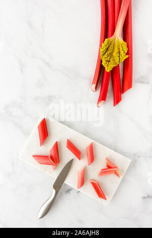 La rhubarbe forcée sur pièces en planche à découper avec couteau et tiges de rhubarbe avec la feuille sur fond de marbre blanc avec l'exemplaire de l'espace. Vue d'en haut. Banque D'Images