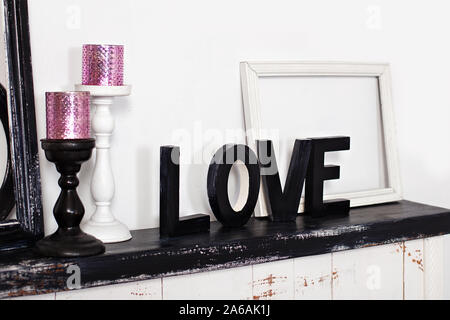 Le mot en bois, c'est l'amour. Sur la cheminée sont deux chandeliers avec des bougies et le mot amour en bois. Amour inscription en lettres en bois. Banque D'Images