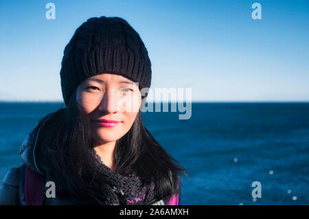 Une femme chinoise portant un chapeau et une veste d'hiver à Newport Rhode island avec l'océan Atlantique à l'arrière-plan. Banque D'Images