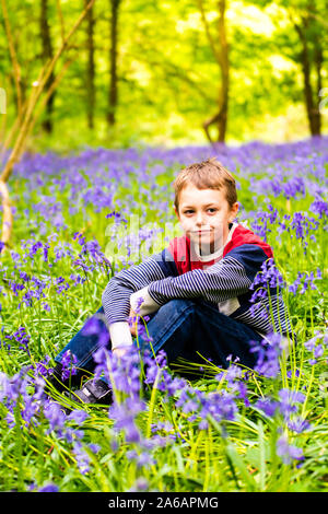 Un beau petit garçon avec le TDAH, l'Autisme, syndrome d'Aspergers est assis et pose pour une photo dans une forêt, bois recouvert de Bluebells, Banque D'Images