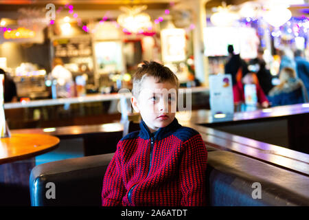 Un beau petit garçon avec le TDAH, l'autisme, syndrome d'apserger est assis dans un restaurant, pub en attente regardant la télévision à Yates à Newcastle Under Lyme Banque D'Images