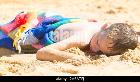 Un beau petit garçon avec TDAH, l'autisme, du syndrome d'Asperger après s'endormir sur la plage sur une belle journée d'été, épuisé, Woodup extérieure, Essex Banque D'Images