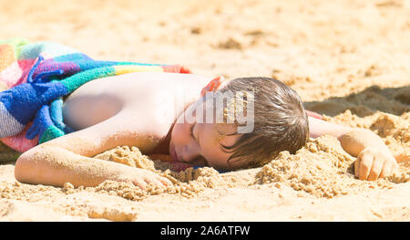 Un beau petit garçon avec TDAH, l'autisme, du syndrome d'Asperger après s'endormir sur la plage sur une belle journée d'été, épuisé, Woodup extérieure, Essex Banque D'Images