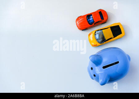 Close up of blue tirelire et deux petites voitures sur fond blanc avec l'exemplaire de l'espace. Coup de frais généraux. Banque D'Images