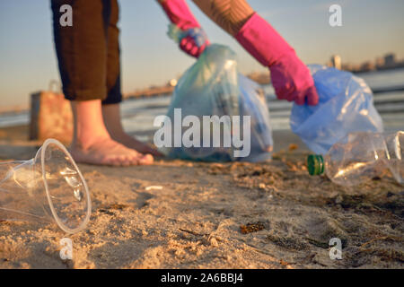 Personne responsable en violet gants de caoutchouc est la marche avec sac à déchets le long d'une plage de la rivière sale et le nettoyage de la corbeille. Les gens et l'écologie. Riv Banque D'Images