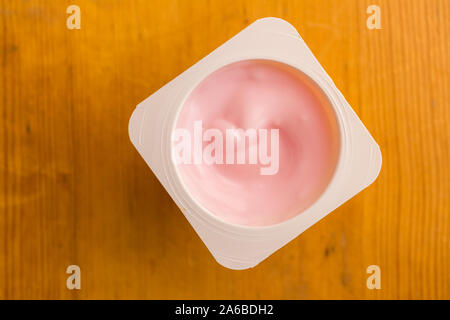 Yogourt aux fraises Rose en petites tasse en plastique isolé sur table en bois - haut voir photo Banque D'Images