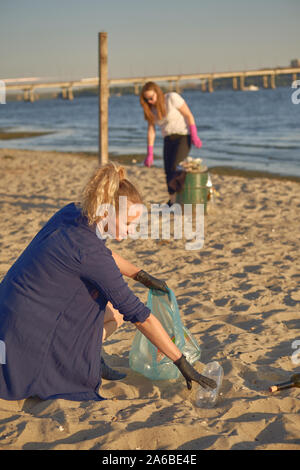 Les jeunes bénévoles en gants noirs sont la marche avec des sacs poubelles le long d'un bord de l'eau sale du fleuve et le nettoyage de la corbeille. Les gens et l'écologie. Les Rivières Banque D'Images