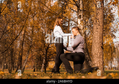 L'amour, couple, relation et concept d'engagement - l'homme à genoux une main embrasse une femme dans le parc en automne Banque D'Images