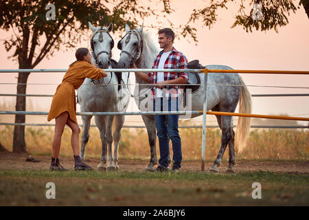 Jeune couple heureux de préparer leurs chevaux pour une randonnée sur farm Banque D'Images