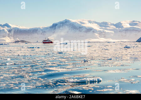 Croisière rouge dérive vapeur loin parmi les icebergs à l'énorme rocher et des glaciers en arrière-plan, la baie de Neco, Antarctique Banque D'Images