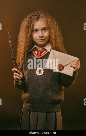 Portrait of a cute enchantress enfant avec de magnifiques longs cheveux bruns vêtu d'un pull bleu marine et gris jupe. Elle est titulaire d'un coup de baguette magique et le Banque D'Images