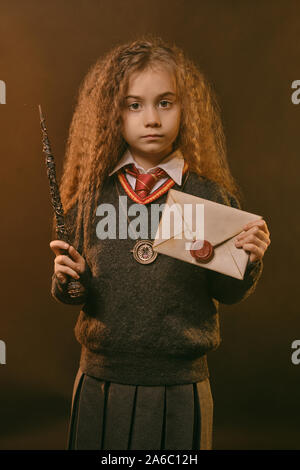 Portrait of a cute kid sorcière avec de magnifiques longs cheveux bruns vêtu d'un pull bleu marine et gris jupe. Elle est titulaire d'un coup de baguette magique et d'une lettre Banque D'Images