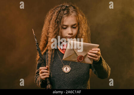 Portrait d'une mignonne petite fille sorcière avec de magnifiques longs cheveux bruns vêtu d'un pull bleu marine, chemise blanche et cravate rouge. Elle est titulaire d'un magic w Banque D'Images