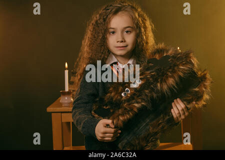 Portrait d'une charmante petite fille sorcière avec de magnifiques longs cheveux bruns vêtu d'un pull bleu marine, chemise blanche et cravate rouge. Elle est debout près de Banque D'Images