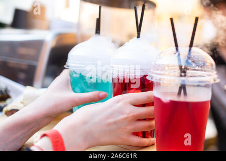 Mains prendre une boisson aux fruits multicolores avec vapeur sortant. Cocktail sans alcool. Close up. Banque D'Images