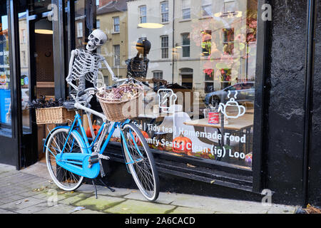 Squelette osseux riding a bicycle bleu debout devant un café décoré pour l'Halloween à Londonderry/Derry Banque D'Images